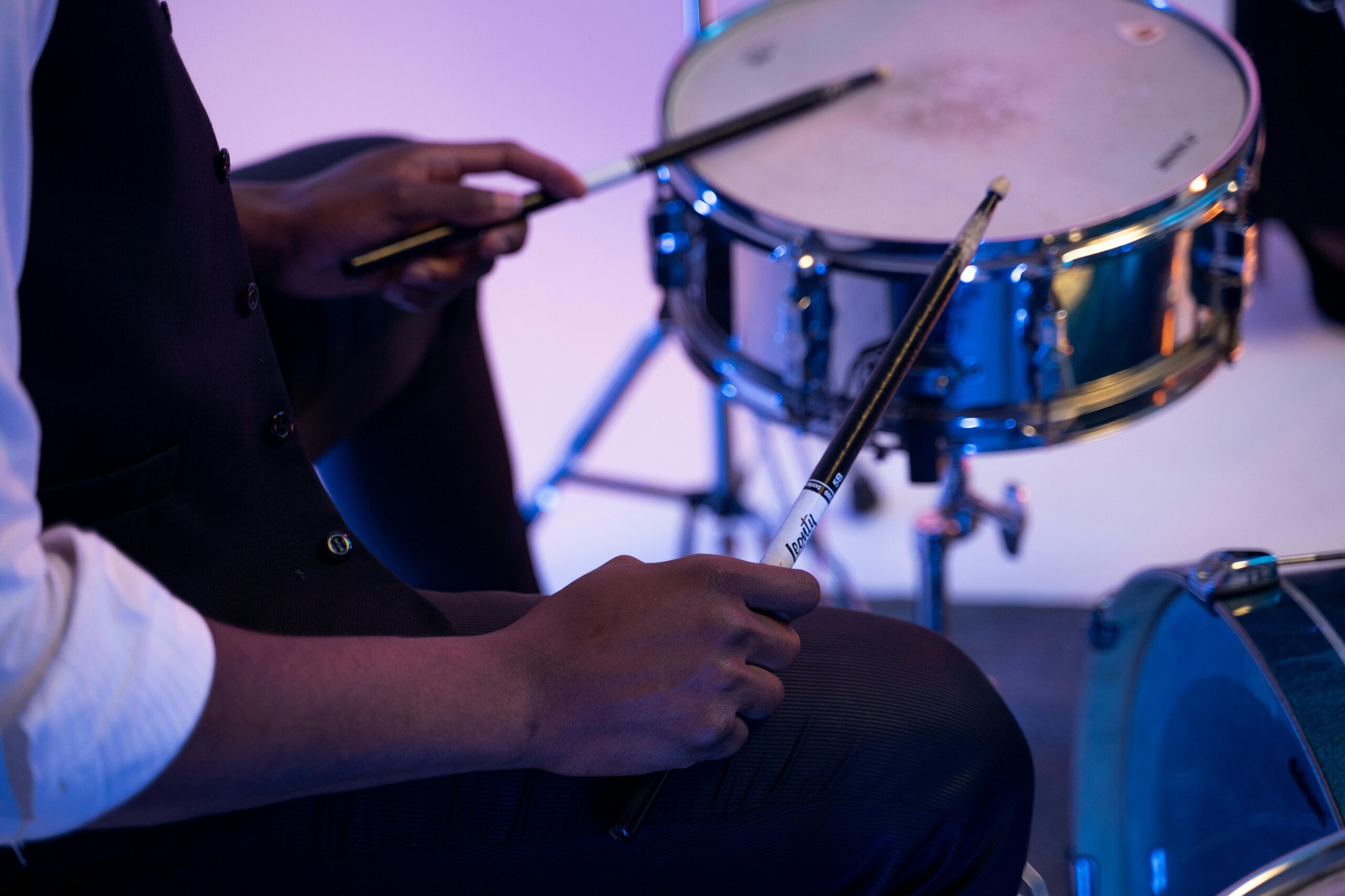 A musician playing a snare drum with drumsticks in a studio setting. Close-up view.