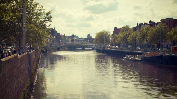 Tranquil city canal scene capturing historic bridge and tree-lined streets under a cloudy sky