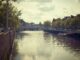 Tranquil city canal scene capturing historic bridge and tree-lined streets under a cloudy sky