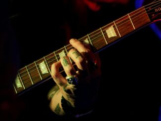Intense focus on tattooed hand playing string instrument in dim lighting, capturing musical passion.