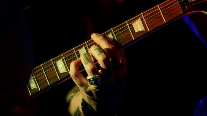 Intense focus on tattooed hand playing string instrument in dim lighting, capturing musical passion.