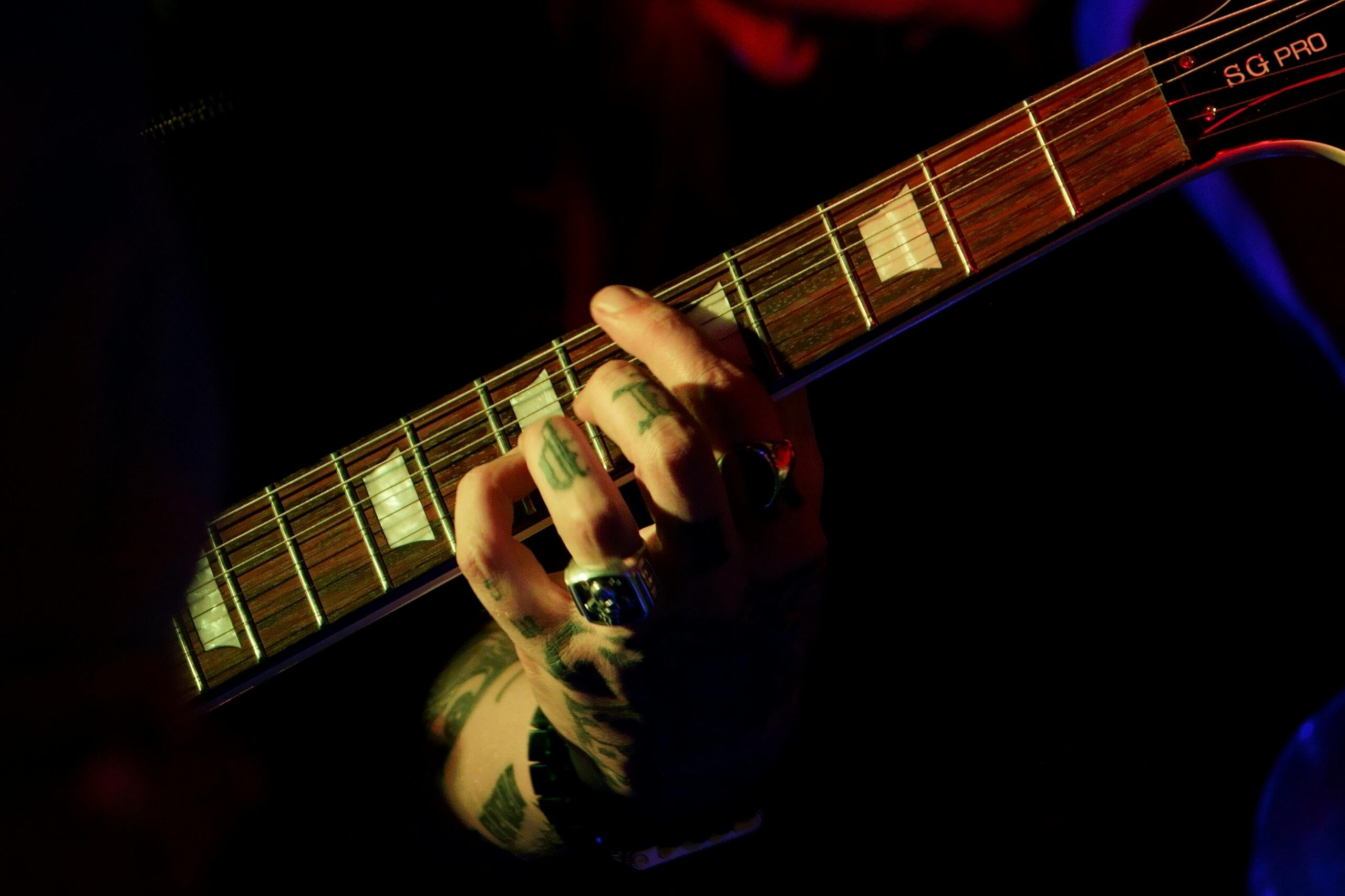 Intense focus on tattooed hand playing string instrument in dim lighting, capturing musical passion.