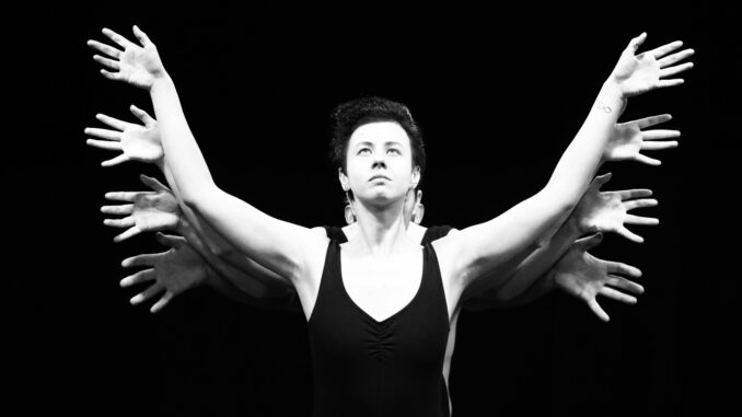 Black and white surreal stage performance featuring a performer with multiple hands.
