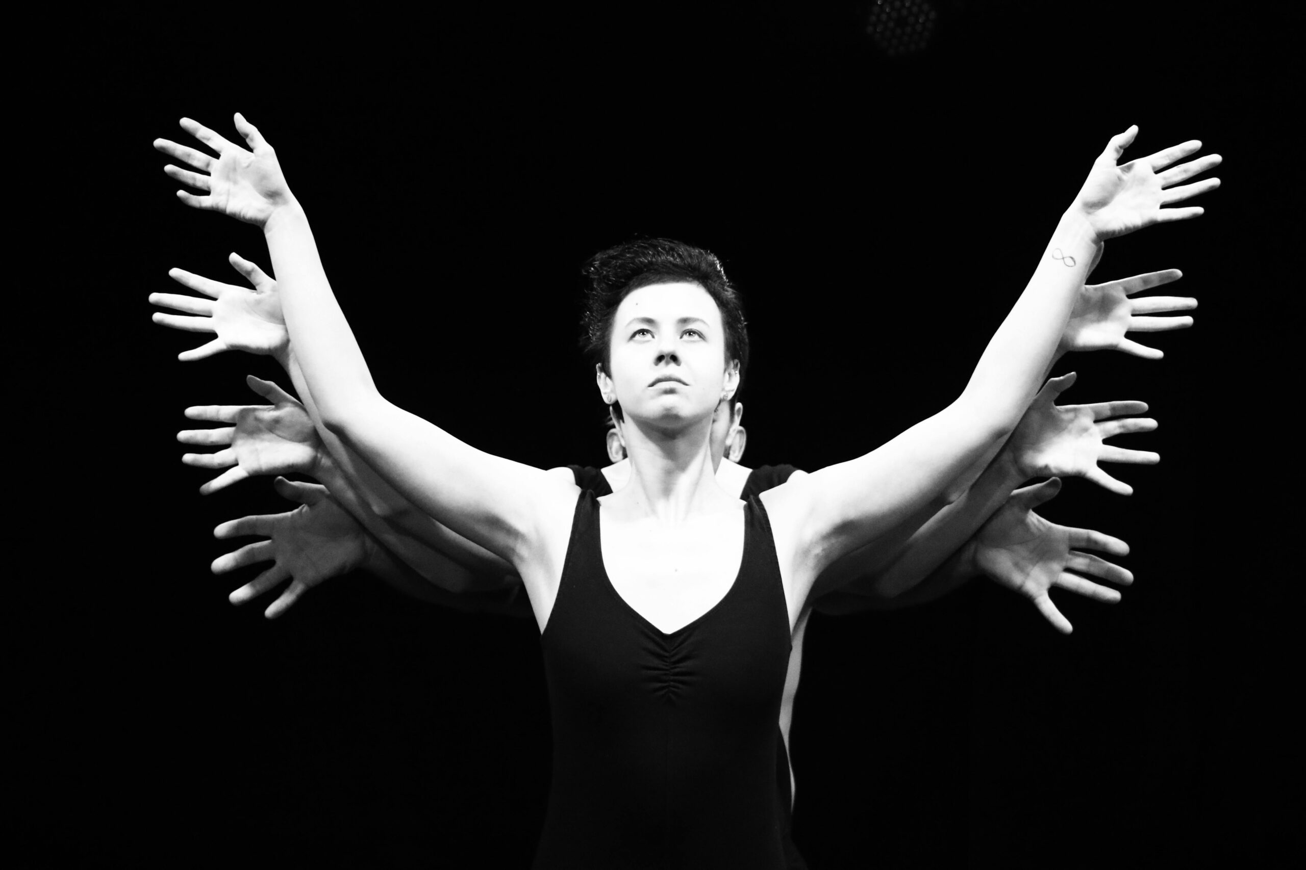 Black and white surreal stage performance featuring a performer with multiple hands.