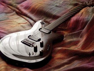 Sleek electric guitar resting on colorful fabric, captured with artistic lighting.