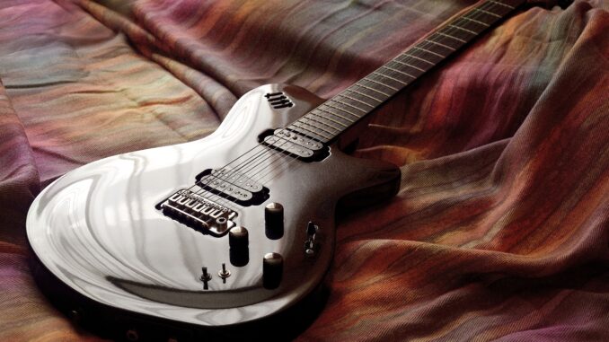 Sleek electric guitar resting on colorful fabric, captured with artistic lighting.