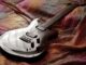 Sleek electric guitar resting on colorful fabric, captured with artistic lighting.