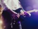 Close-up of a musician passionately playing an electric guitar under stage lights.