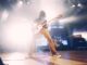 Dynamic low angle shot of a guitarist performing live on stage with vibrant lighting effects.