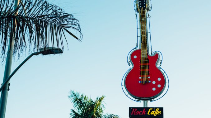 A bright red guitar sign at Rock Cafe with tropical palm trees and clear skies.