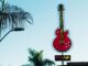 A bright red guitar sign at Rock Cafe with tropical palm trees and clear skies.