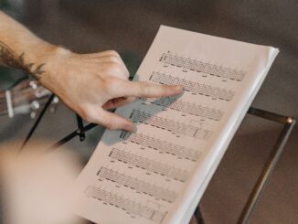 Close-up of a musician pointing at guitar sheet music on a stand indoors.
