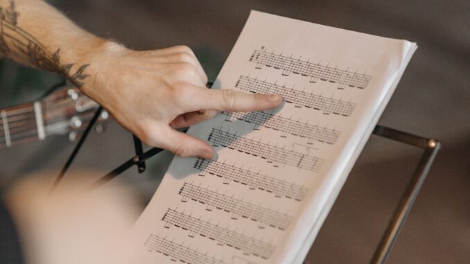 Close-up of a musician pointing at guitar sheet music on a stand indoors.