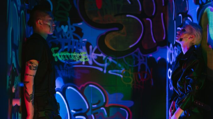 Two individuals celebrating street style in a graffiti-lit room under neon lights.