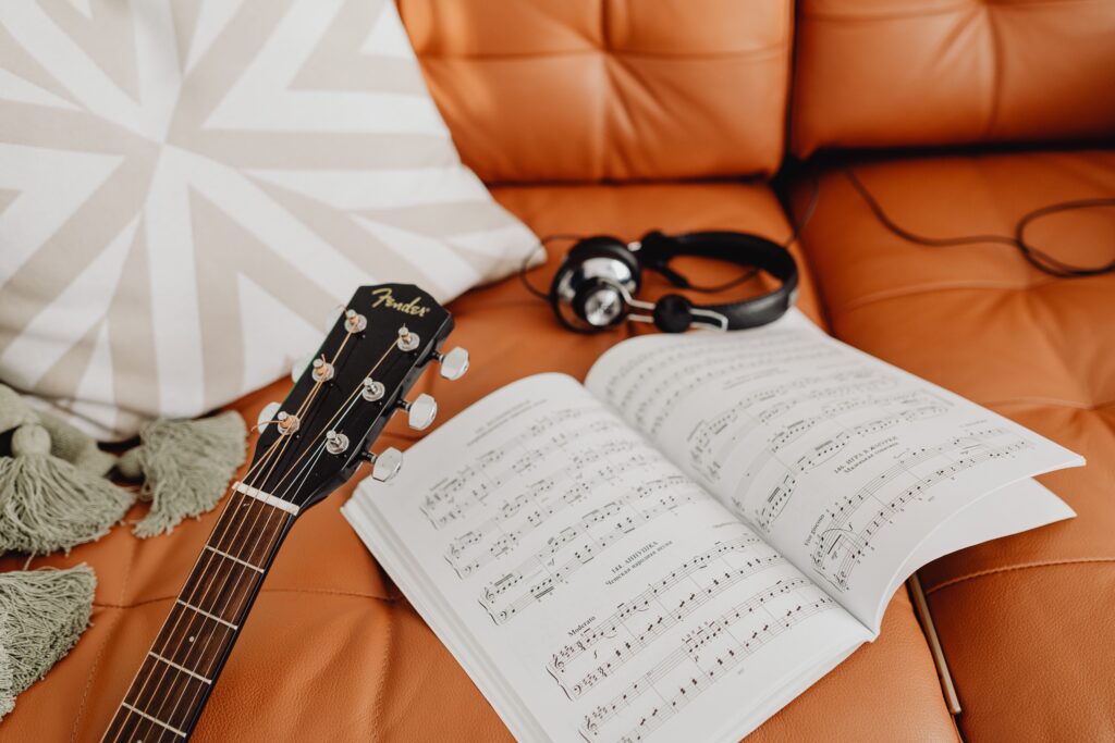 A cozy music composition setup with a guitar, headphones, and sheet music on a sofa.