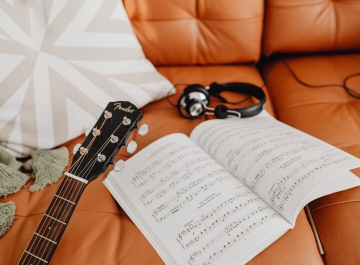 A cozy music composition setup with a guitar, headphones, and sheet music on a sofa.