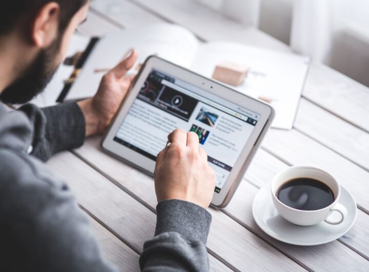 A man uses a tablet to browse news while enjoying a cup of coffee, stylus in hand.