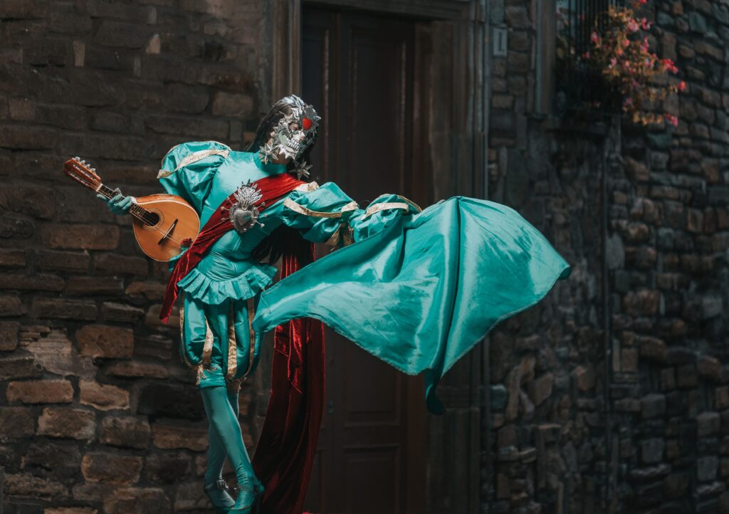 Colorful costumed performer brings Venice carnival charm with a ukulele on a cobblestone street.