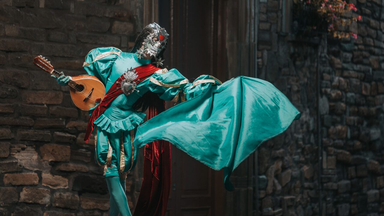 Colorful costumed performer brings Venice carnival charm with a ukulele on a cobblestone street.