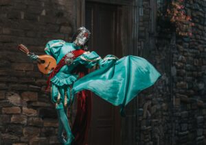 Colorful costumed performer brings Venice carnival charm with a ukulele on a cobblestone street.
