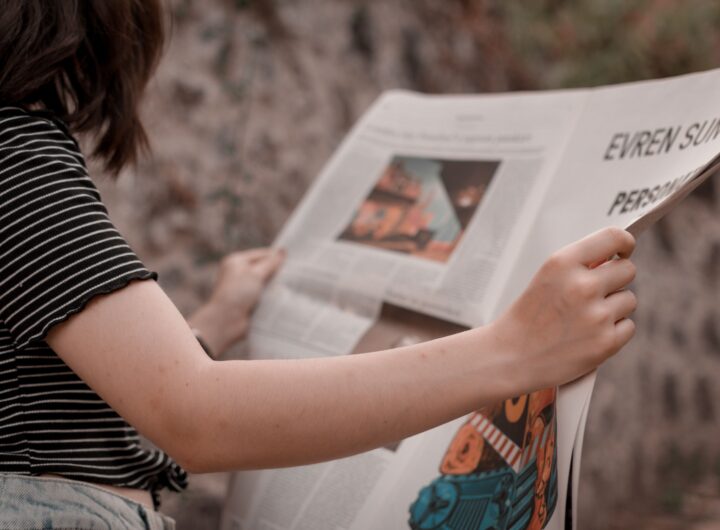 A woman holding a newspaper while sitting outside, enjoying a leisurely read.